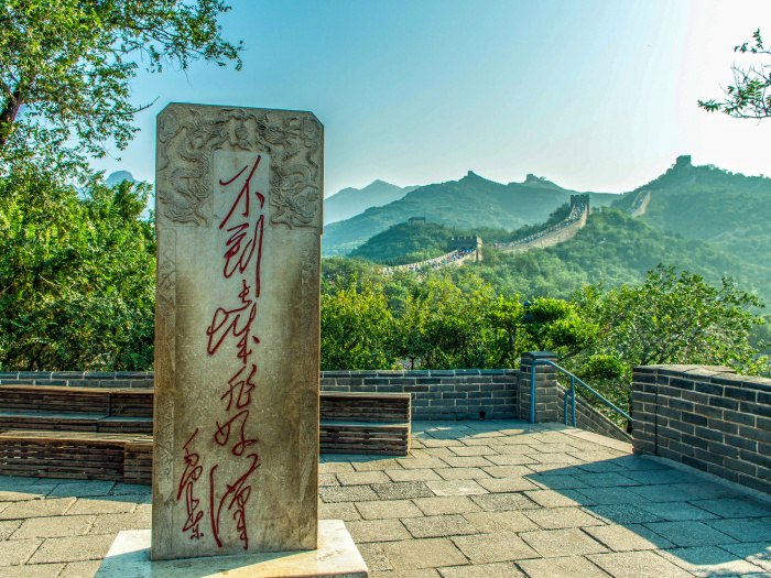 A stone inscription beside a Great Wall walkway with green mountains beyond